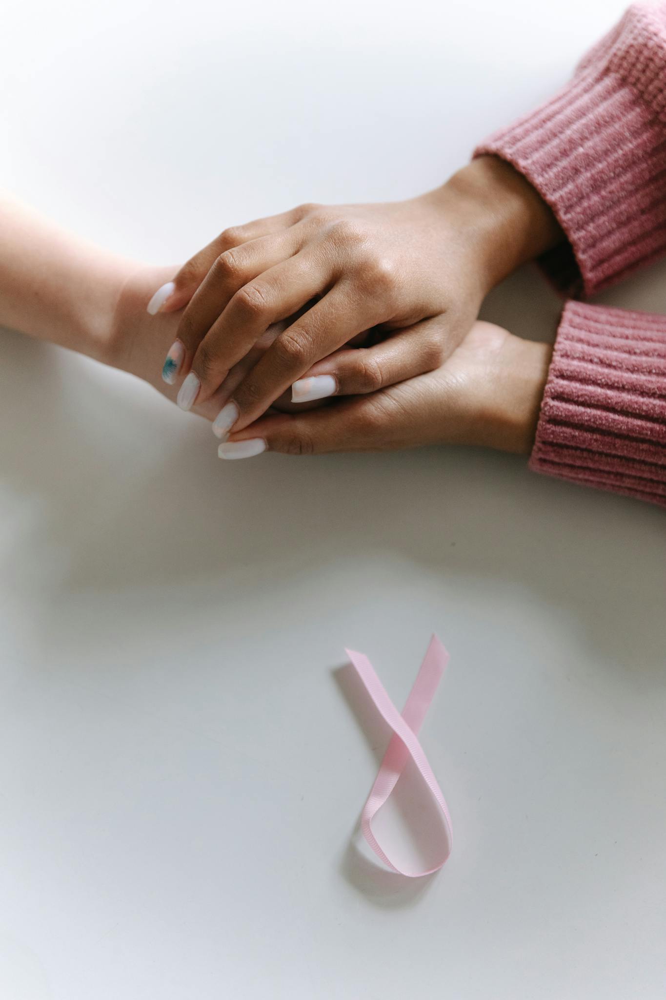 Close-up of two hands holding with a pink ribbon symbolizing cancer awareness.