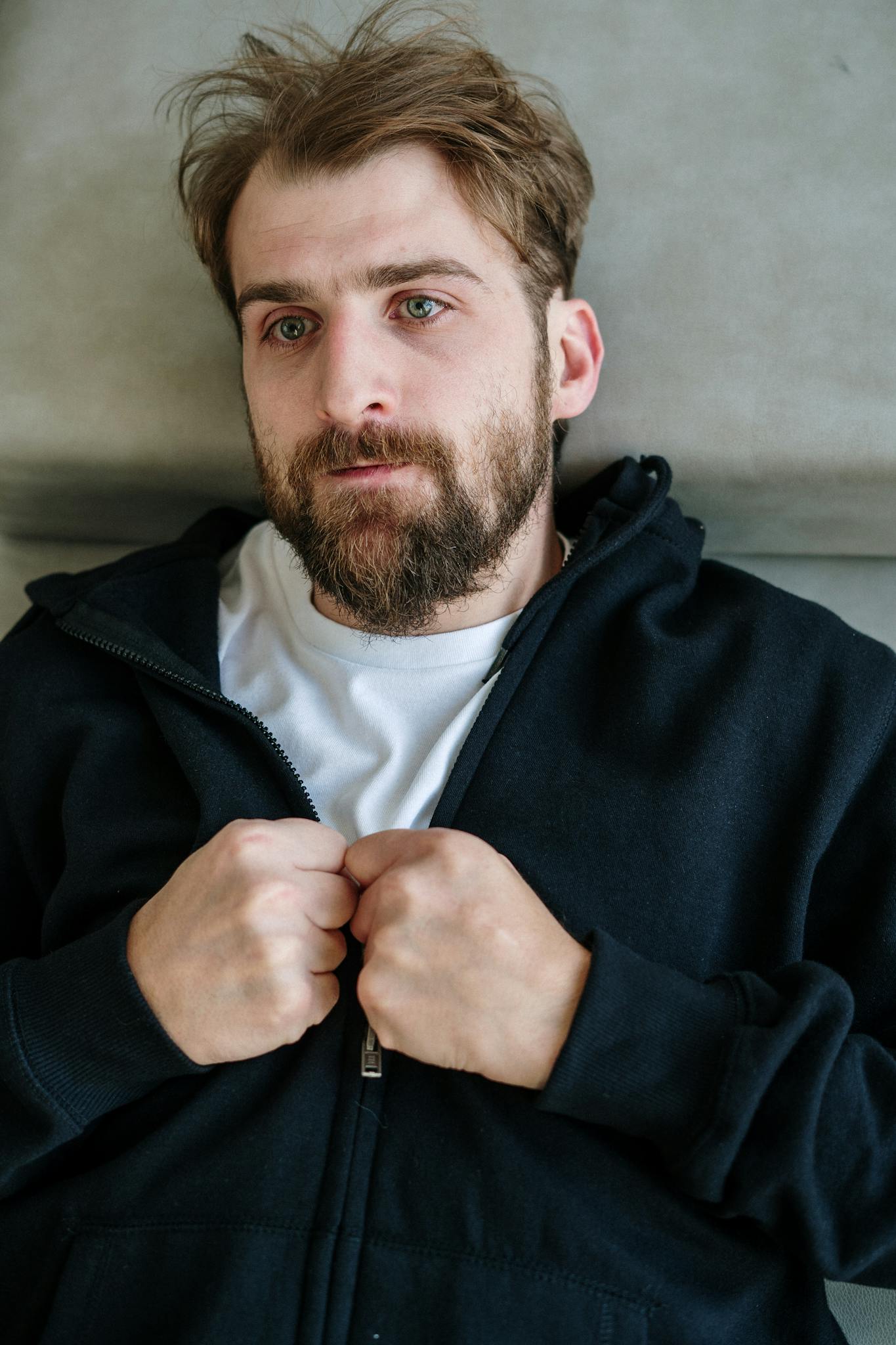 Bearded man lying on a sofa, appearing pensive and introspective indoors.